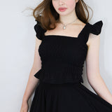 Model wearing a black shirred flutter sleeve cotton blouse with a matching black skirt.