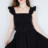 Model wearing a black shirred flutter sleeve cotton blouse with a matching black skirt.