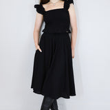 Model wearing a black shirred flutter sleeve cotton blouse with a matching black skirt.