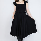 Model wearing a black shirred flutter sleeve cotton blouse with a matching black skirt.