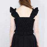 Model wearing a black shirred flutter sleeve cotton blouse with a matching black skirt.
