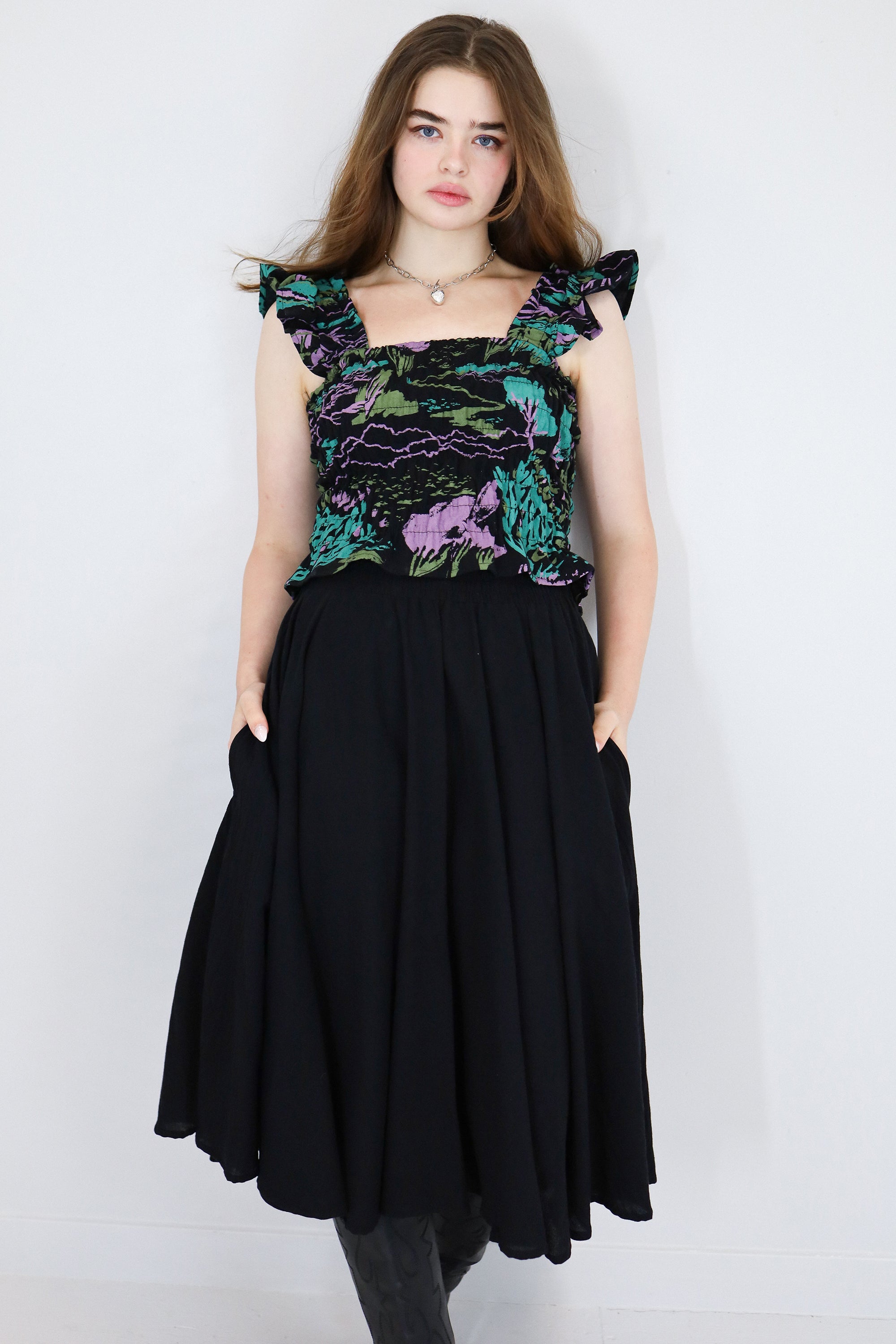 Model wearing a black floral shirred flutter sleeve cotton blouse featuring a colourful landscape print paired with a matching black skirt.