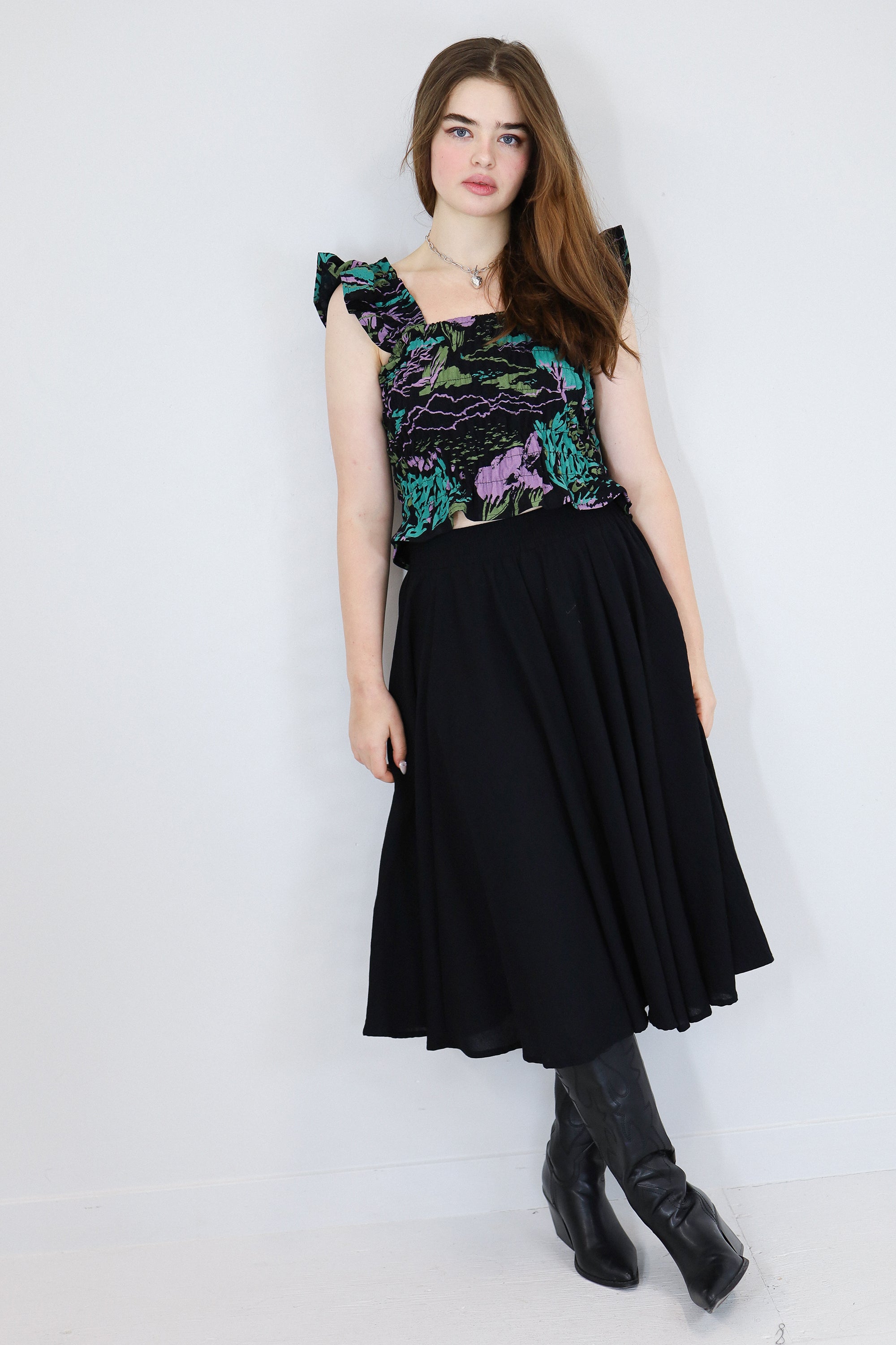 Model wearing a black floral shirred flutter sleeve cotton blouse featuring a colourful landscape print paired with a matching black skirt.