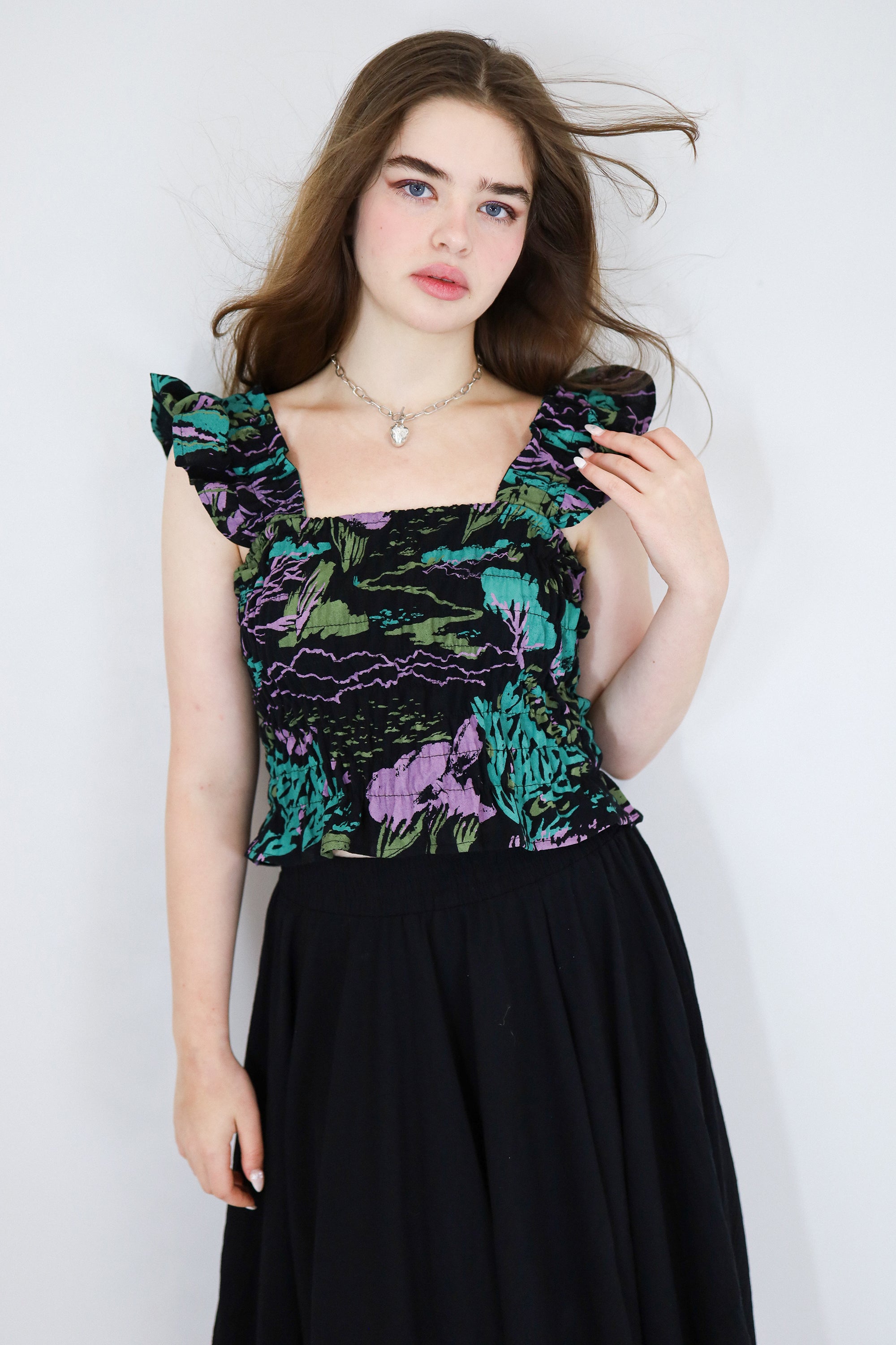 Model wearing a black floral shirred flutter sleeve cotton blouse featuring a colourful landscape print paired with a matching black skirt.
