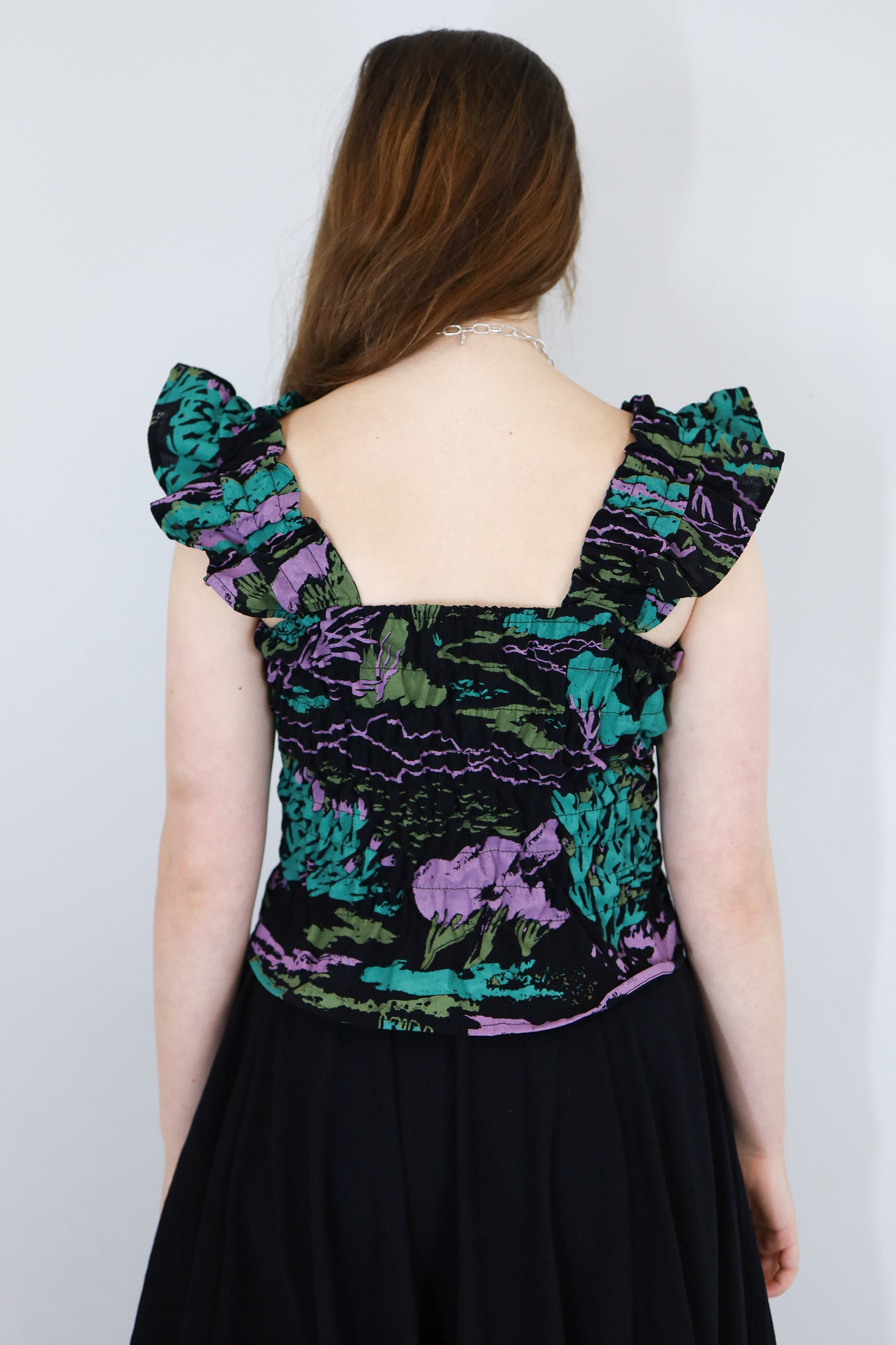 Model wearing a black floral shirred flutter sleeve cotton blouse featuring a colourful landscape print paired with a matching black skirt.