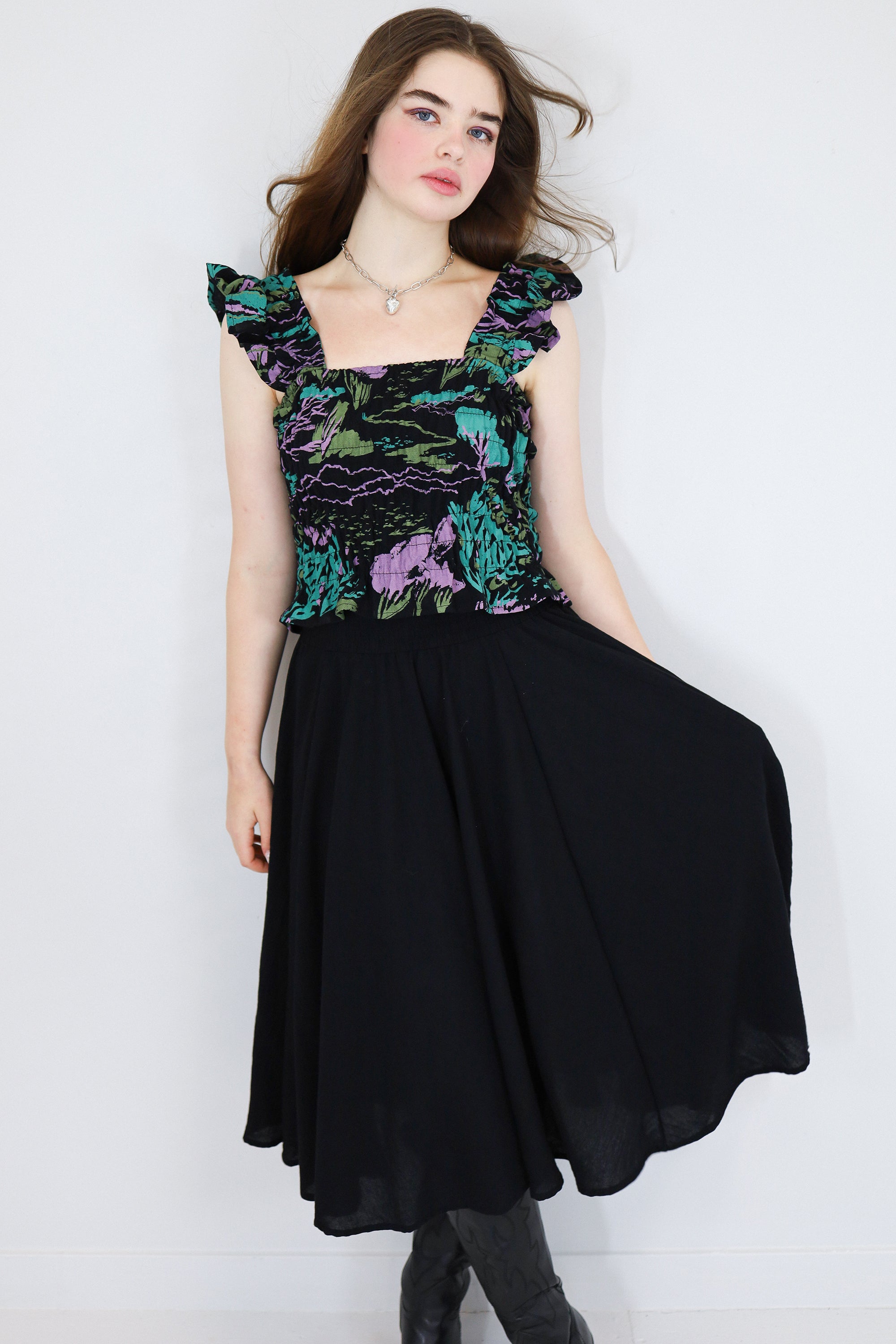 Model wearing a black floral shirred flutter sleeve cotton blouse featuring a colourful landscape print paired with a matching black skirt.