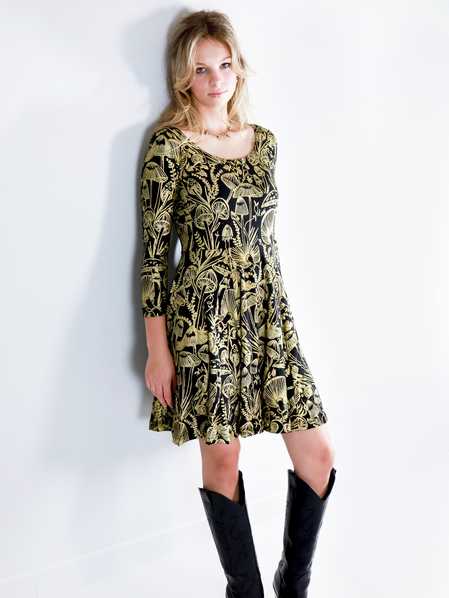 Model wearing a gold on black mushroom dress in a fit and flare twirl styled with black cowboy boots.
