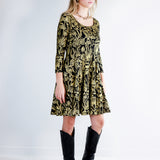 Model wearing a gold on black mushroom dress in a fit and flare twirl styled with black cowboy boots