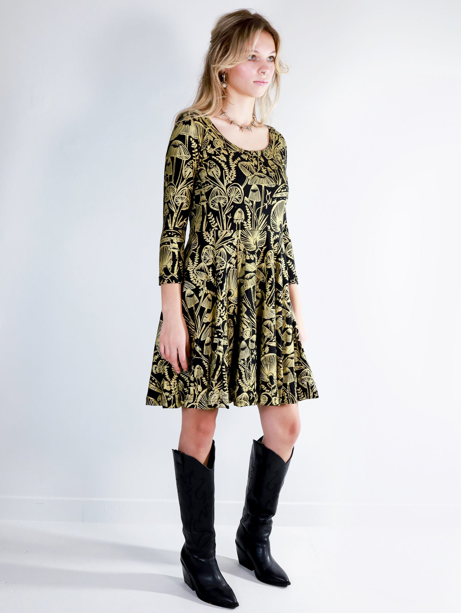 Model wearing a gold on black mushroom dress in a fit and flare twirl styled with black cowboy boots