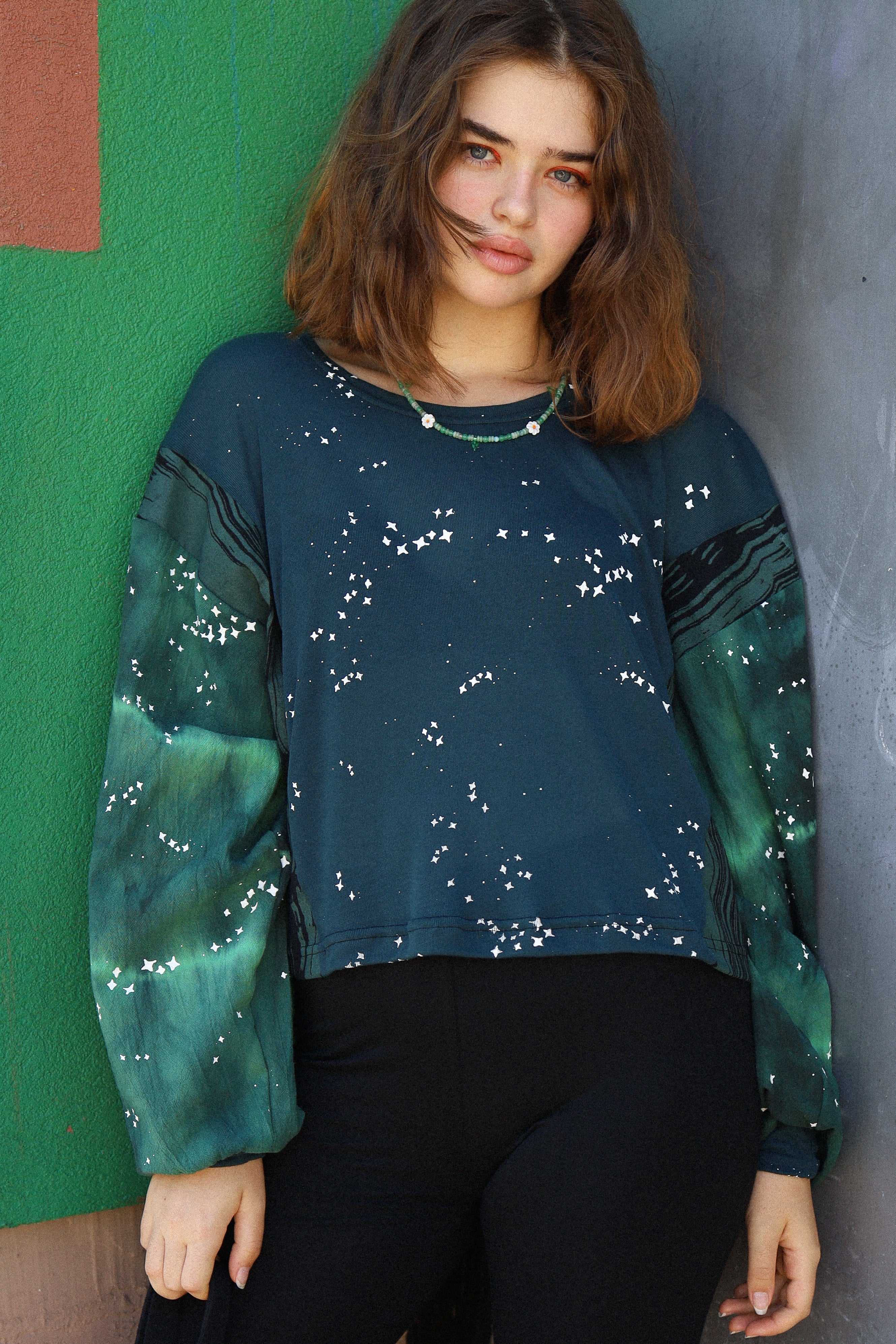 Woman wearing a green and blue patterned sweater against a colorful wall.