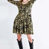 Model wearing a gold on black mushroom dress in a fit and flare twirl styled with black cowboy boots.