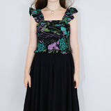 Model wearing a black floral shirred flutter sleeve cotton blouse featuring a colourful landscape print paired with a matching black skirt.