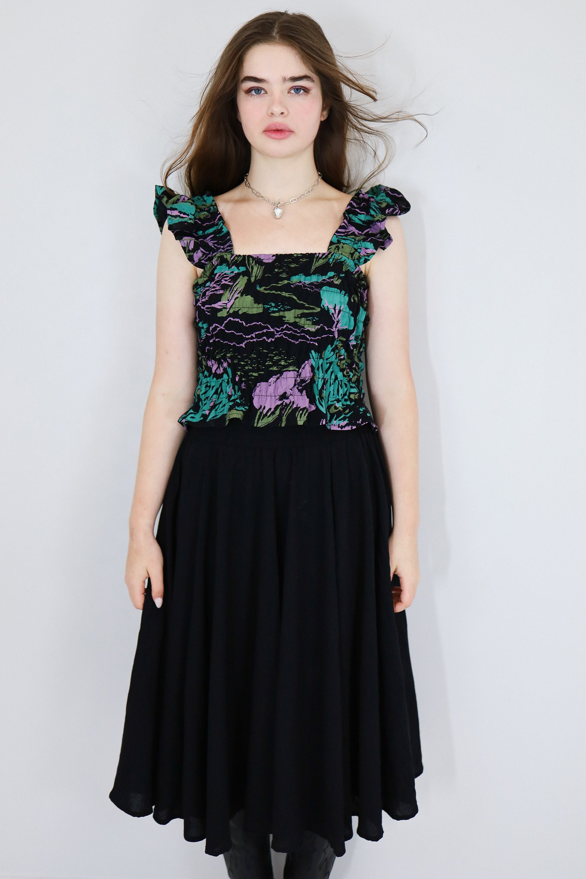 Model wearing a black floral shirred flutter sleeve cotton blouse featuring a colourful landscape print paired with a matching black skirt.