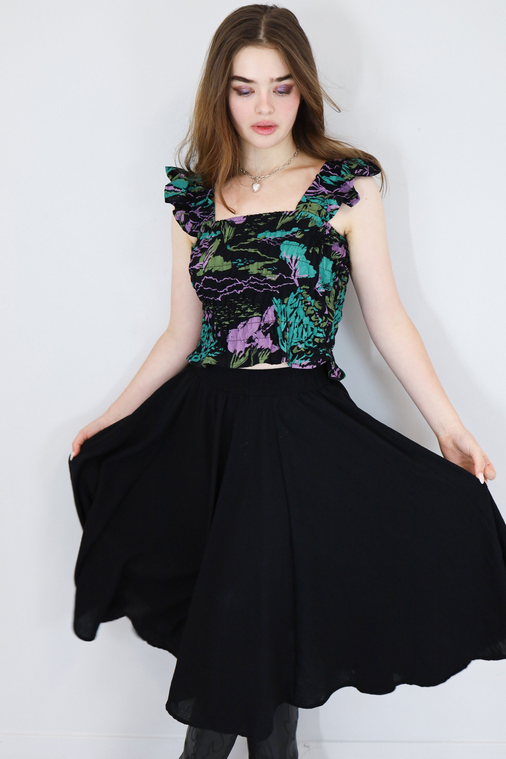 Model wearing a black floral shirred flutter sleeve cotton blouse featuring a colourful landscape print paired with a matching black skirt.