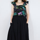 Model wearing a black floral shirred flutter sleeve cotton blouse featuring a colourful landscape print paired with a matching black skirt.
