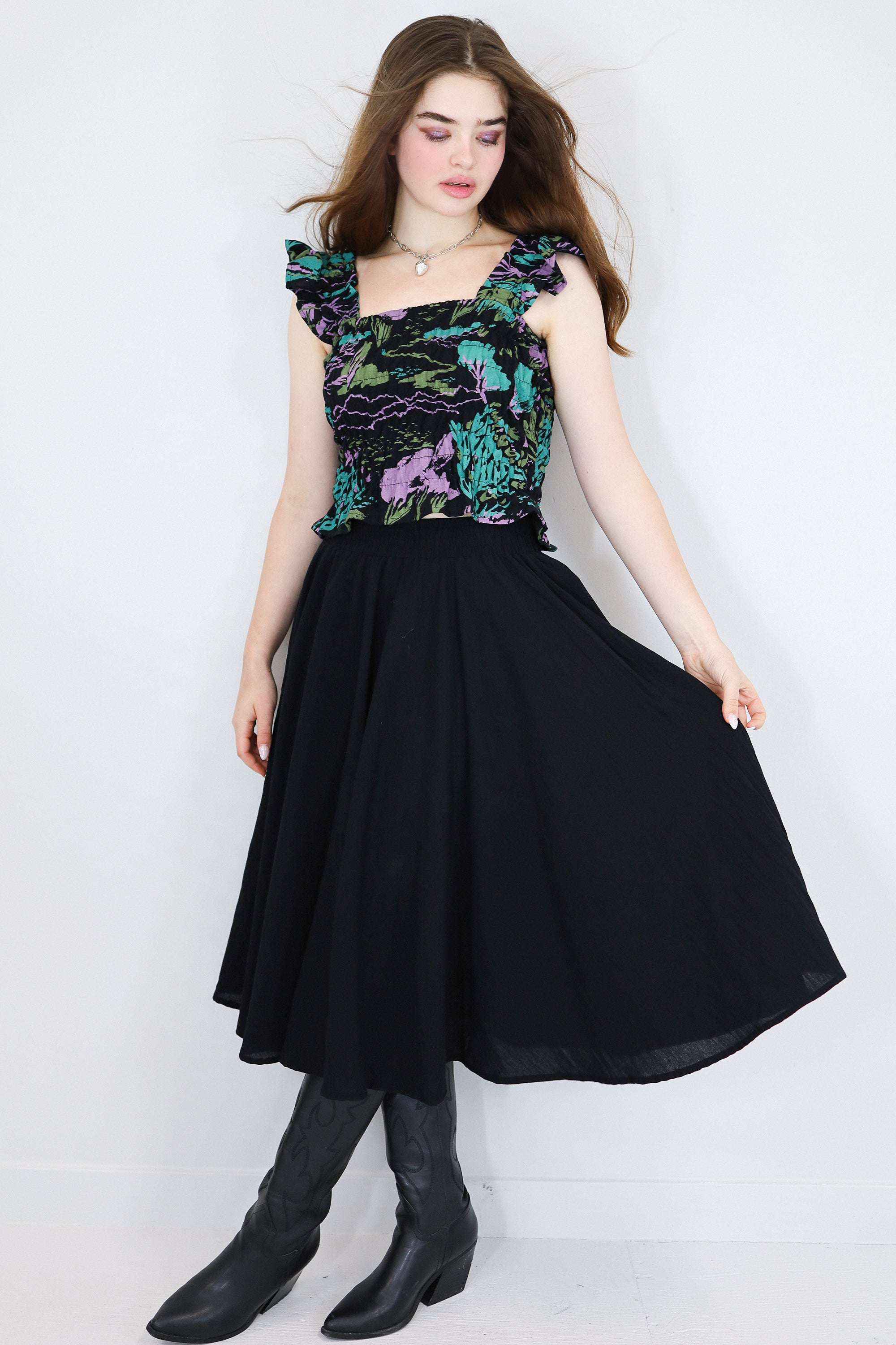 Model wearing a black floral shirred flutter sleeve cotton blouse featuring a colourful landscape print paired with a matching black skirt.