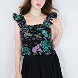 Model wearing a black floral shirred flutter sleeve cotton blouse featuring a colourful landscape print paired with a matching black skirt.