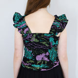 Model wearing a black floral shirred flutter sleeve cotton blouse featuring a colourful landscape print paired with a matching black skirt.