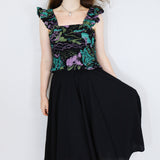 Model wearing a black floral shirred flutter sleeve cotton blouse featuring a colourful landscape print paired with a matching black skirt.