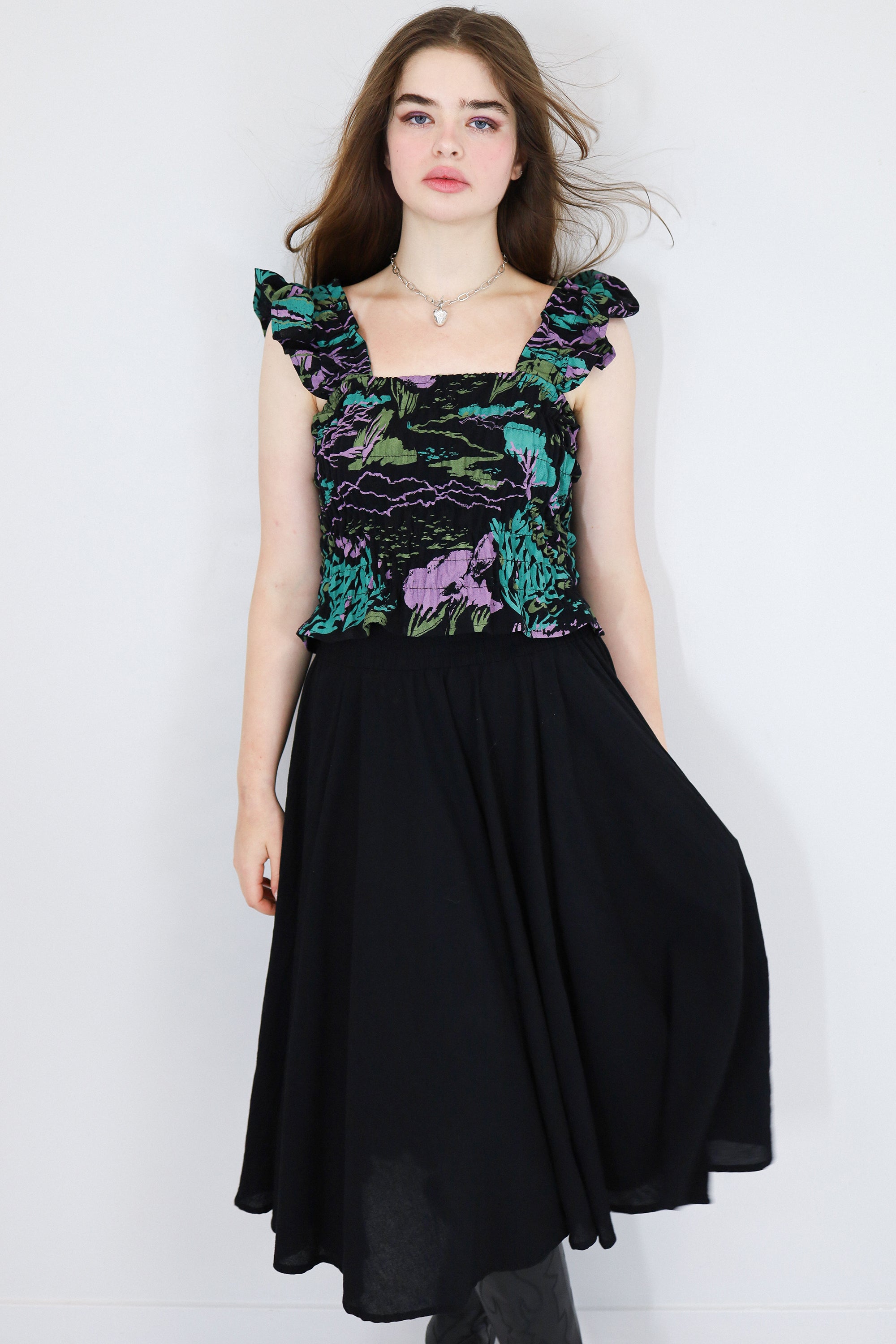 Model wearing a black floral shirred flutter sleeve cotton blouse featuring a colourful landscape print paired with a matching black skirt.