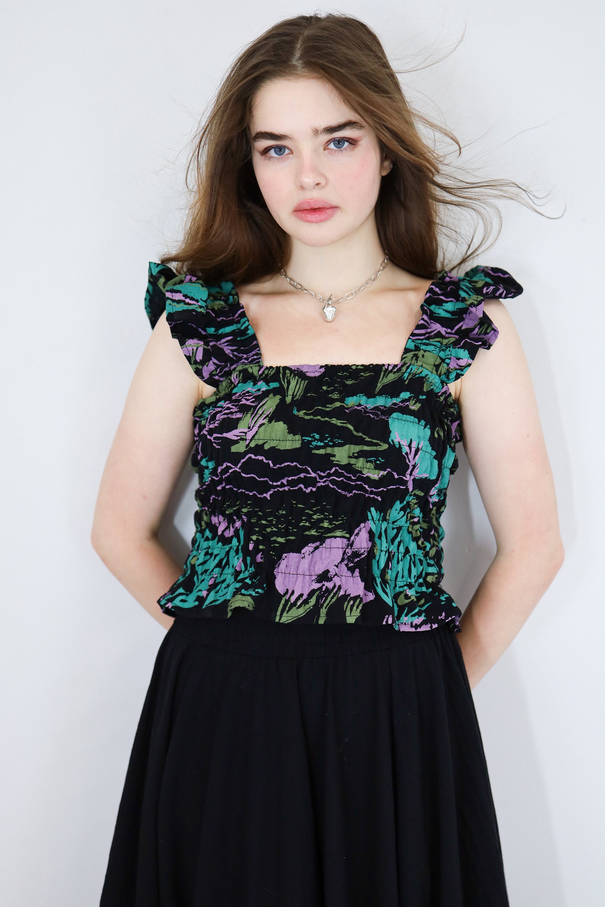 Model wearing a black floral shirred flutter sleeve cotton blouse featuring a colourful landscape print paired with a matching black skirt.