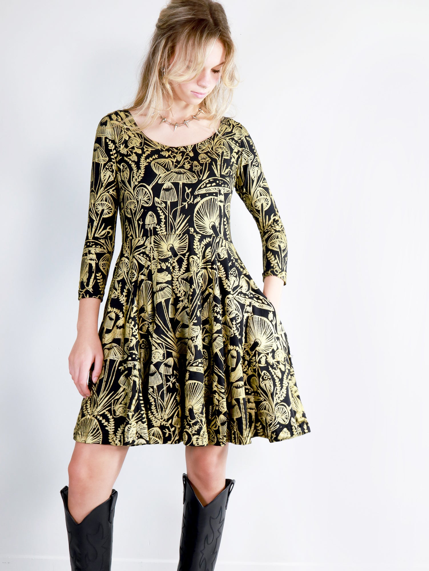 Model wearing a gold on black mushroom dress in a fit and flare twirl styled with black cowboy boots.