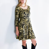 Model wearing a gold on black mushroom dress in a fit and flare twirl styled with black cowboy boots.

