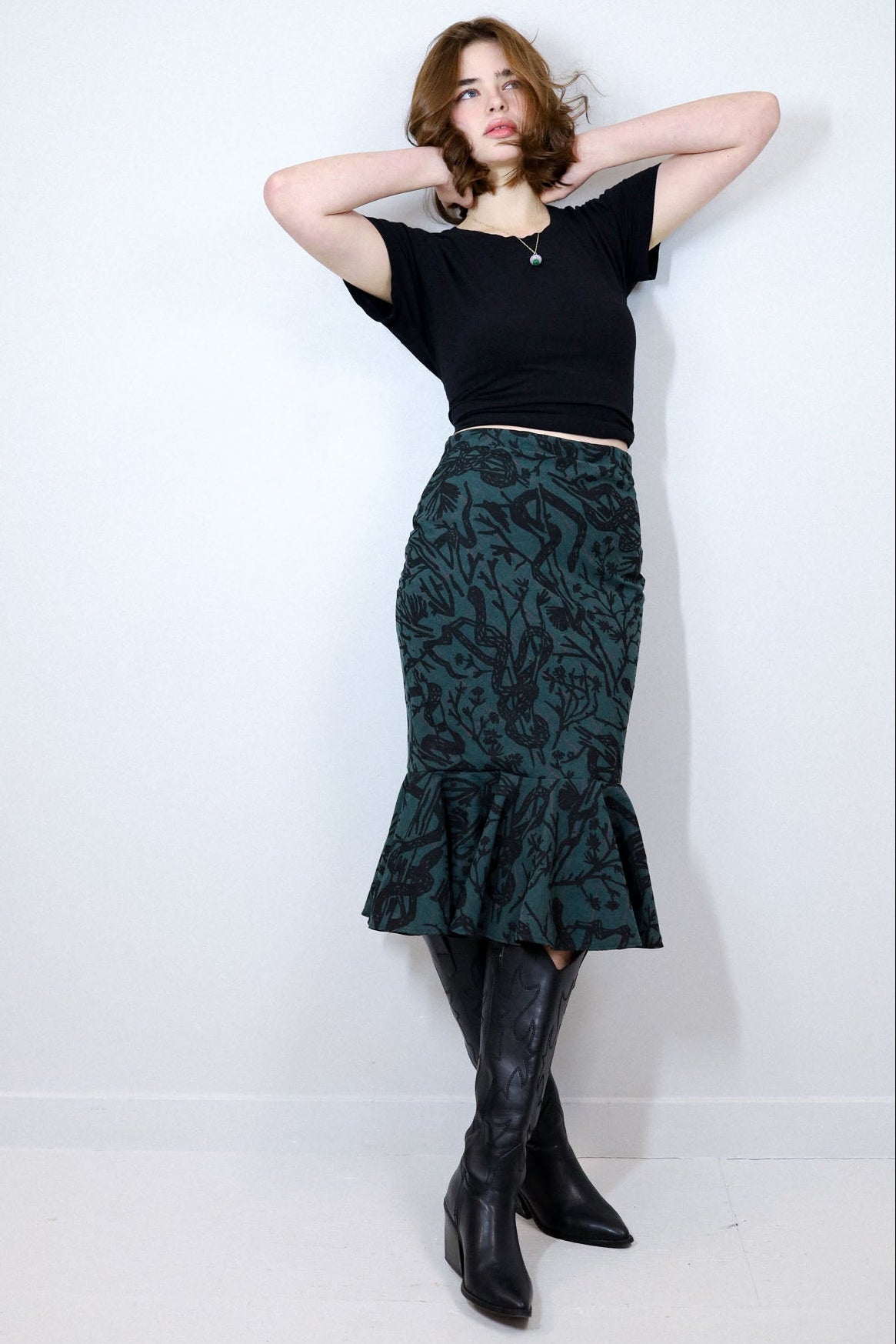 Woman wearing a black top and green patterned skirt against a white background