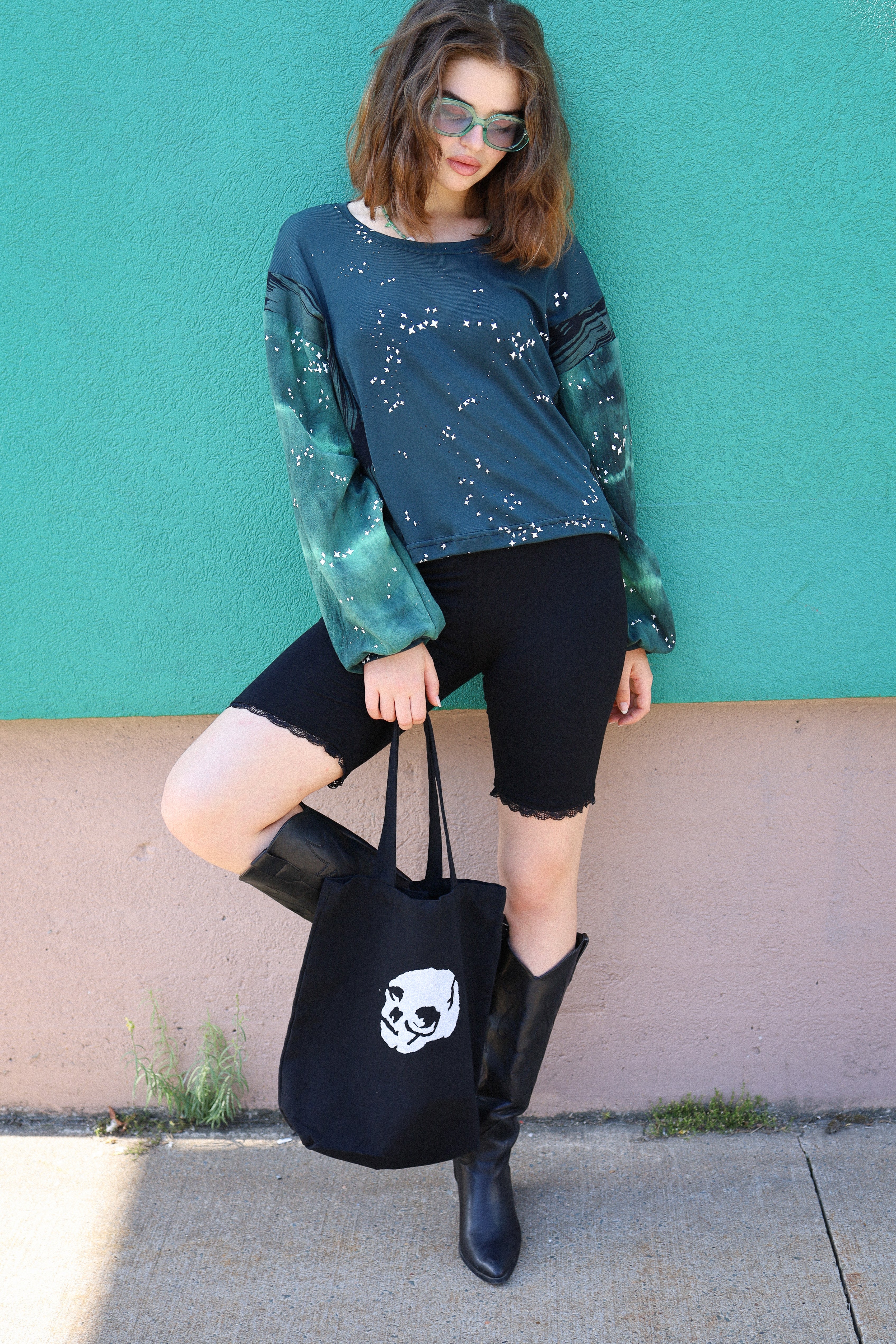 Woman holding a black tote bag with a white design against a teal wall.