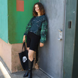 Woman standing against a green wall with a black door, holding a black bag with a white design.