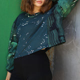 Woman wearing a green and black patterned top against a green wall.