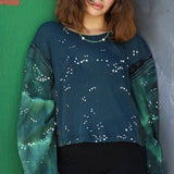 Woman wearing a green and blue patterned sweater against a colorful wall.