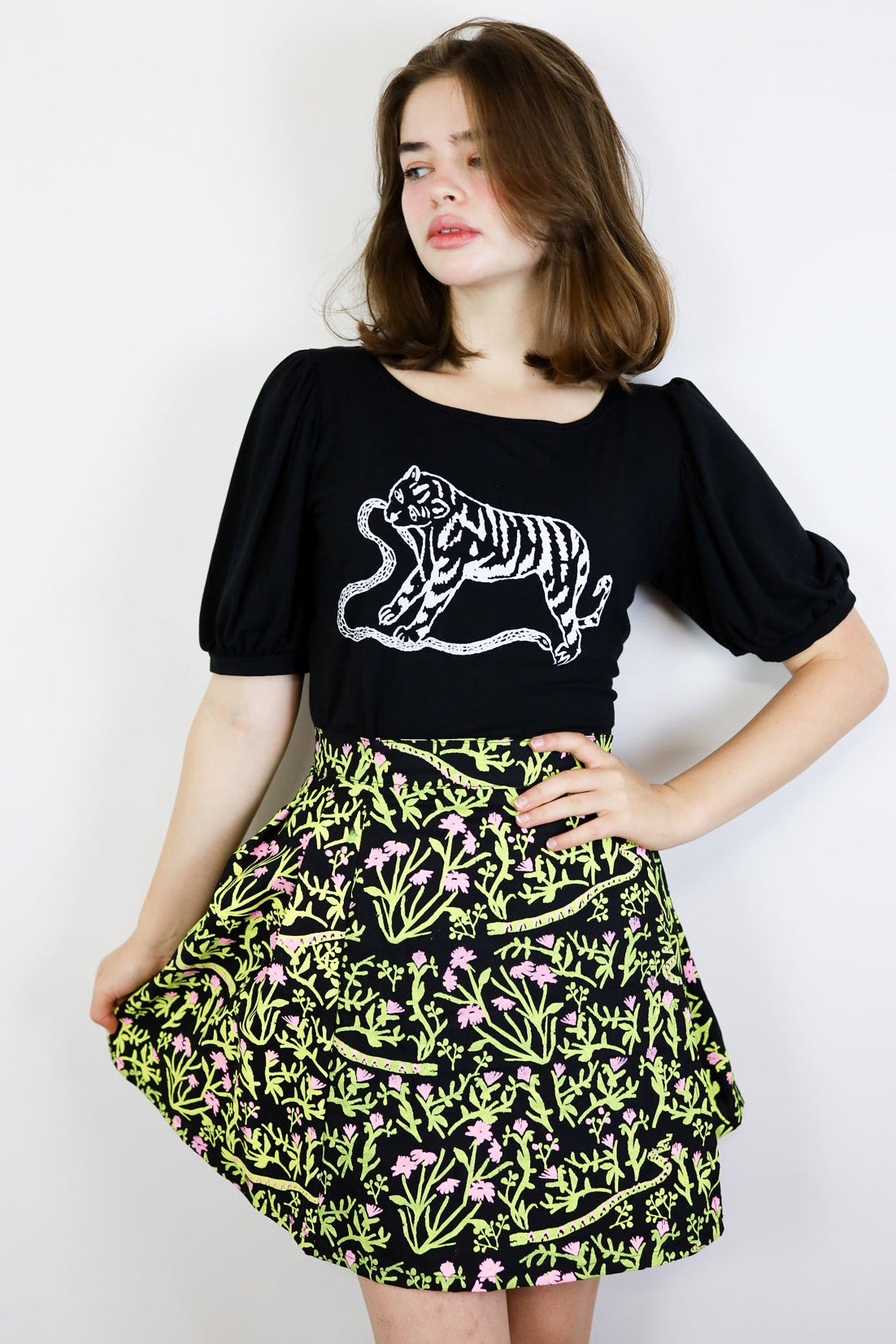 Woman wearing a black t-shirt with a tiger design and a floral skirt on a white background
