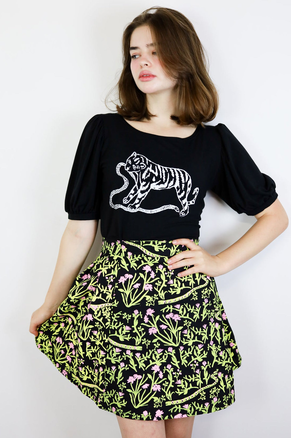 Woman wearing a black t-shirt with a tiger design and a floral skirt on a white background