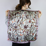 Person holding a large floral and bird patterned scarf against a white background