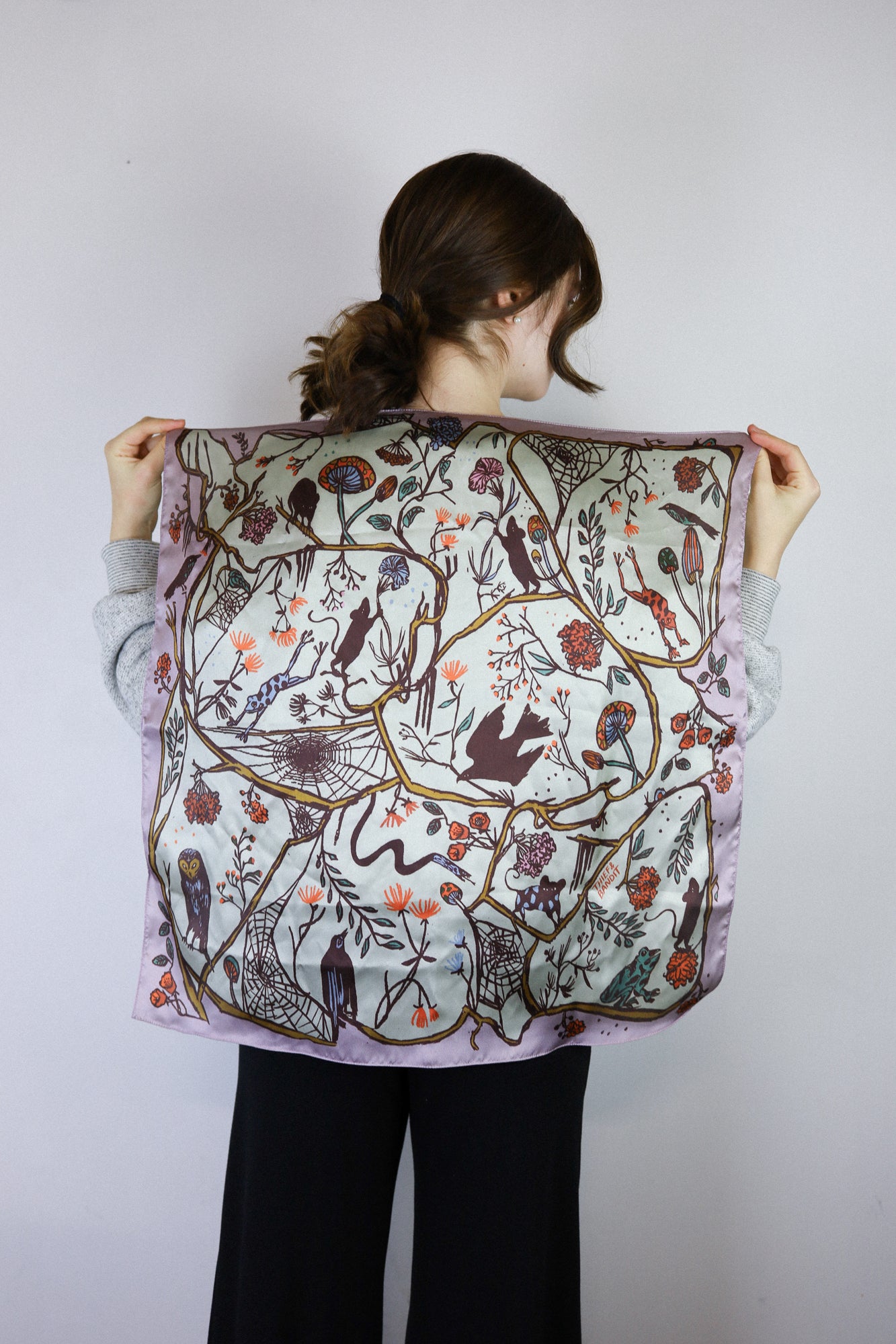 Person holding a large floral and bird patterned scarf against a white background