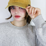 Person wearing a mustard yellow cap with a black cat design against a white background