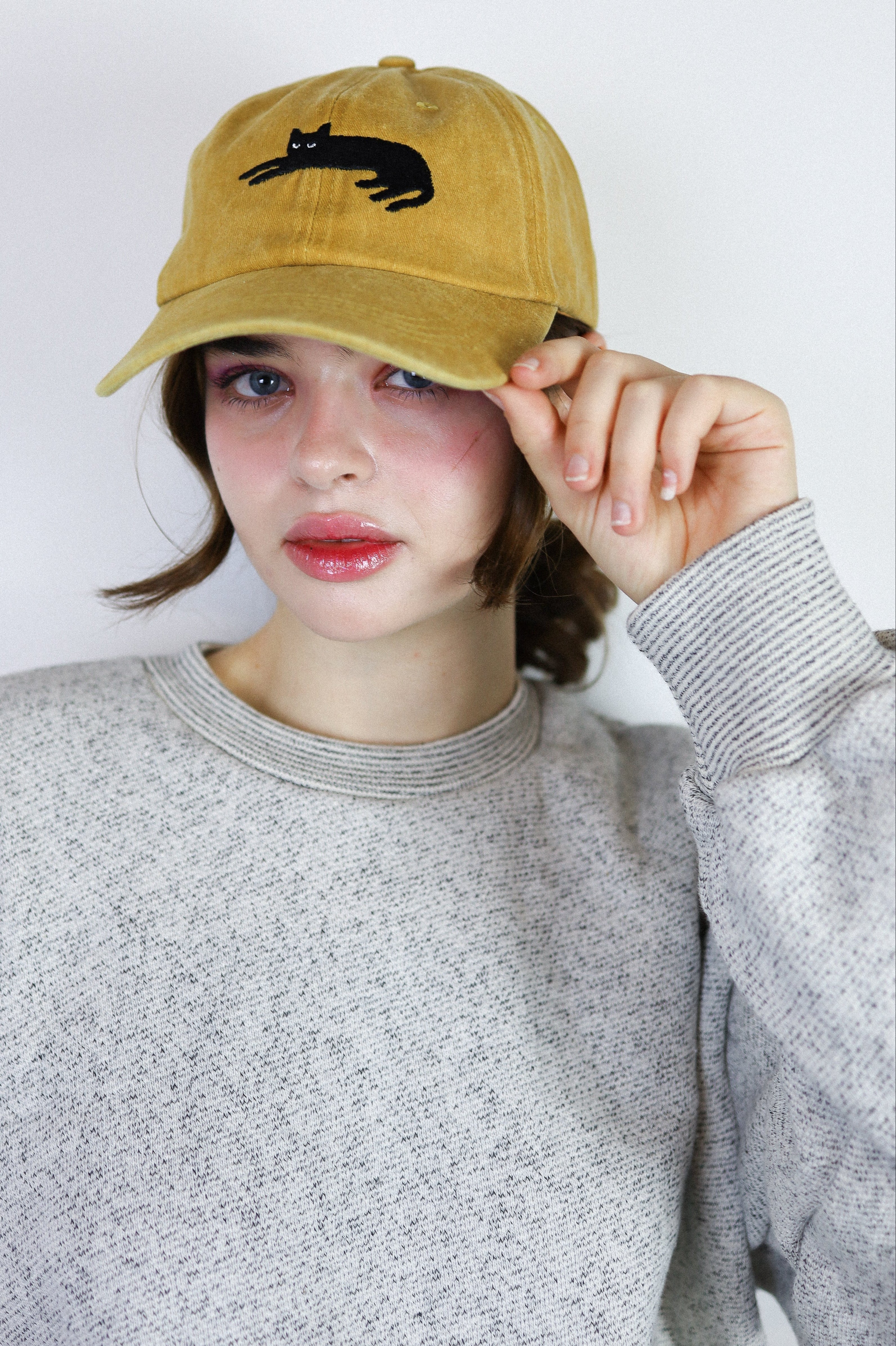 Person wearing a mustard yellow cap with a black cat design against a white background