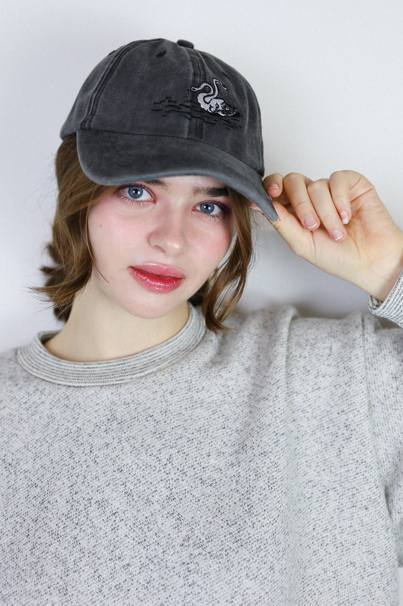 Person wearing a dark gray cap with a logo on a plain background