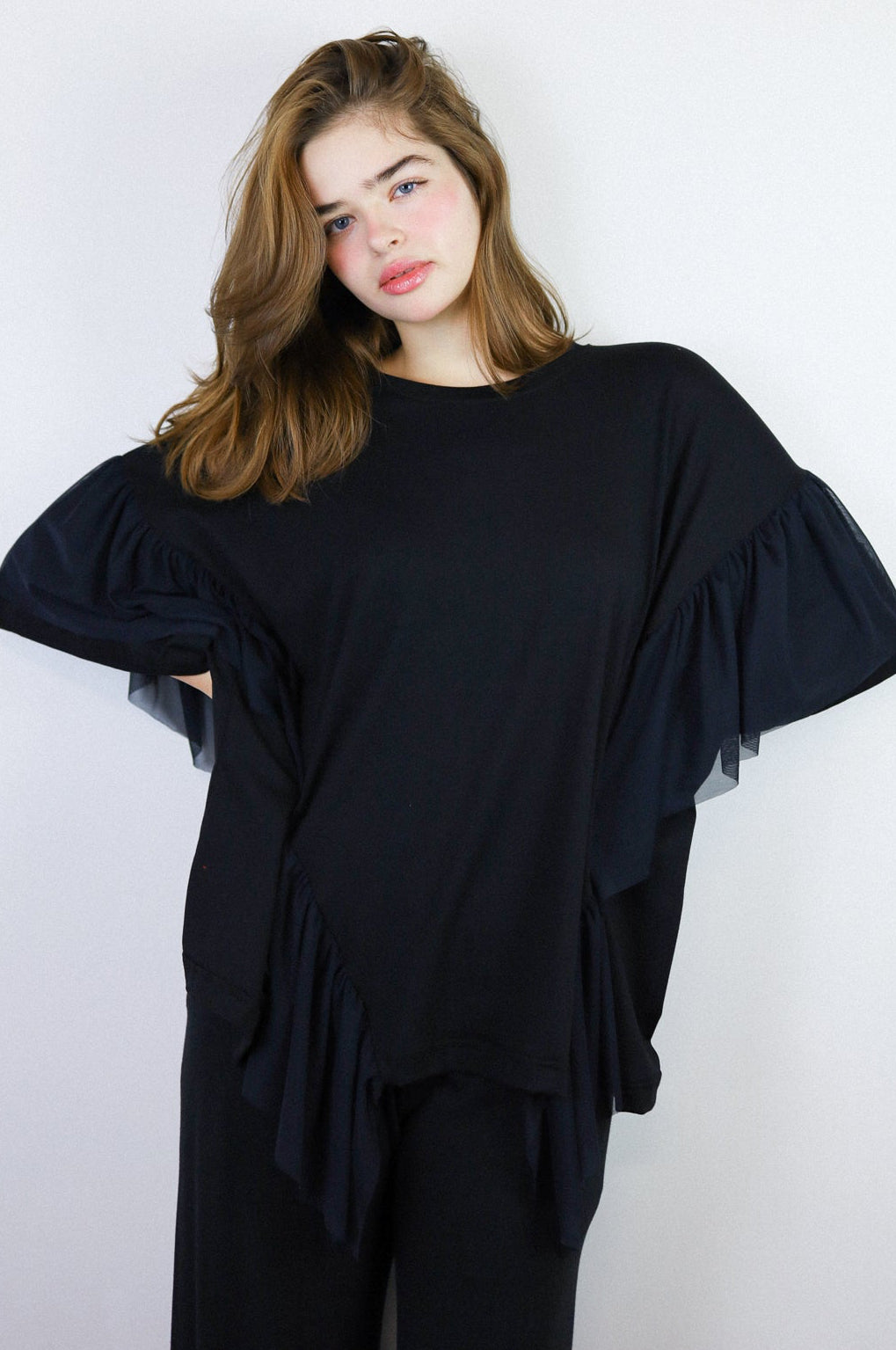 Person wearing a black outfit with ruffled sleeves against a white background