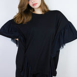 Person wearing a black outfit with ruffled sleeves against a white background