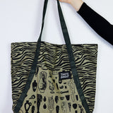 Tote bag with zebra pattern and black text held by a hand on a white background