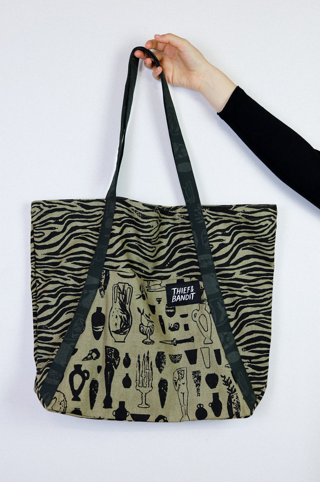 Tote bag with zebra pattern and black text held by a hand on a white background