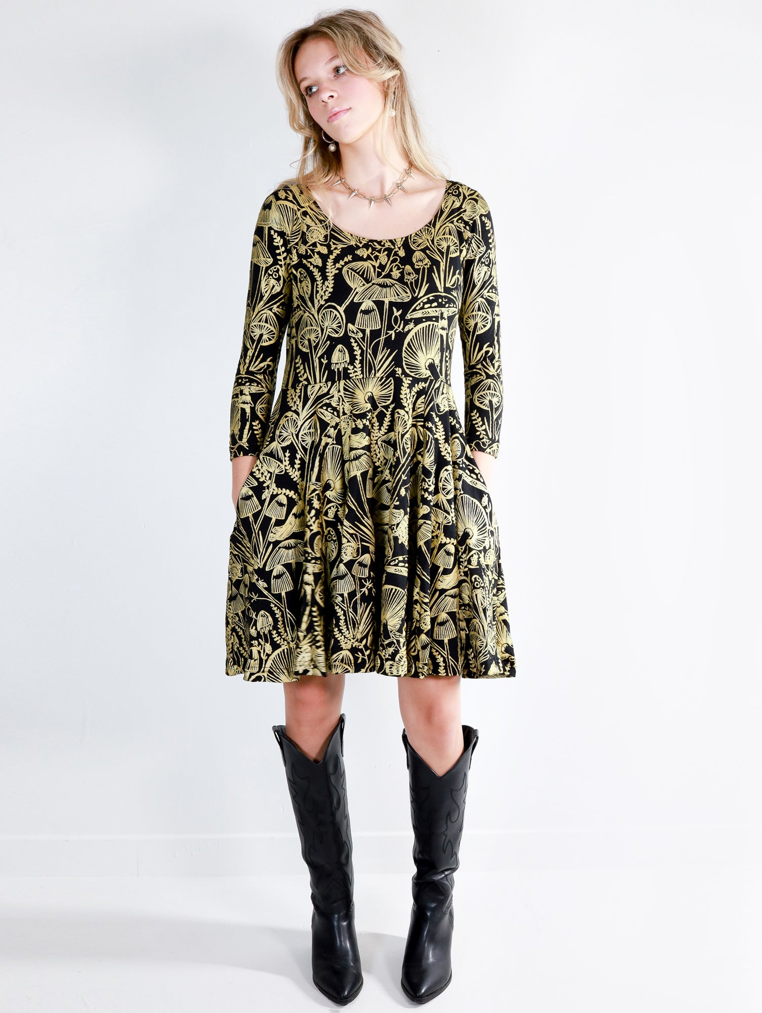 Model wearing a gold on black mushroom dress in a fit and flare twirl styled with black cowboy boots.
