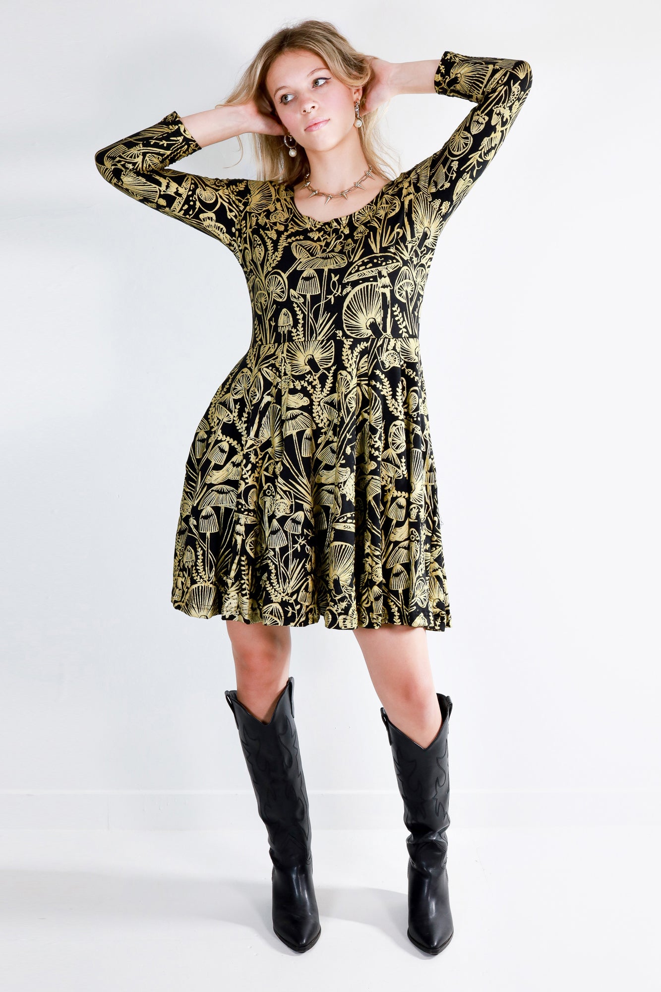 Model wearing a gold on black mushroom dress in a fit and flare twirl styled with black cowboy boots.
