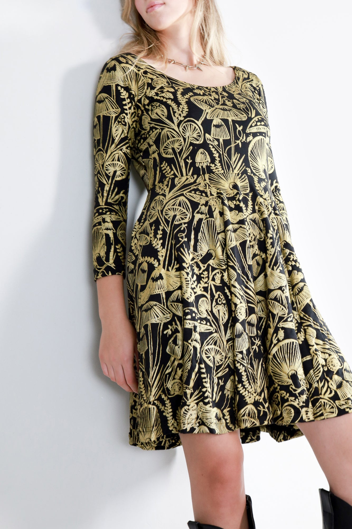 Model wearing a gold on black mushroom dress in a fit and flare twirl styled with black cowboy boots.
